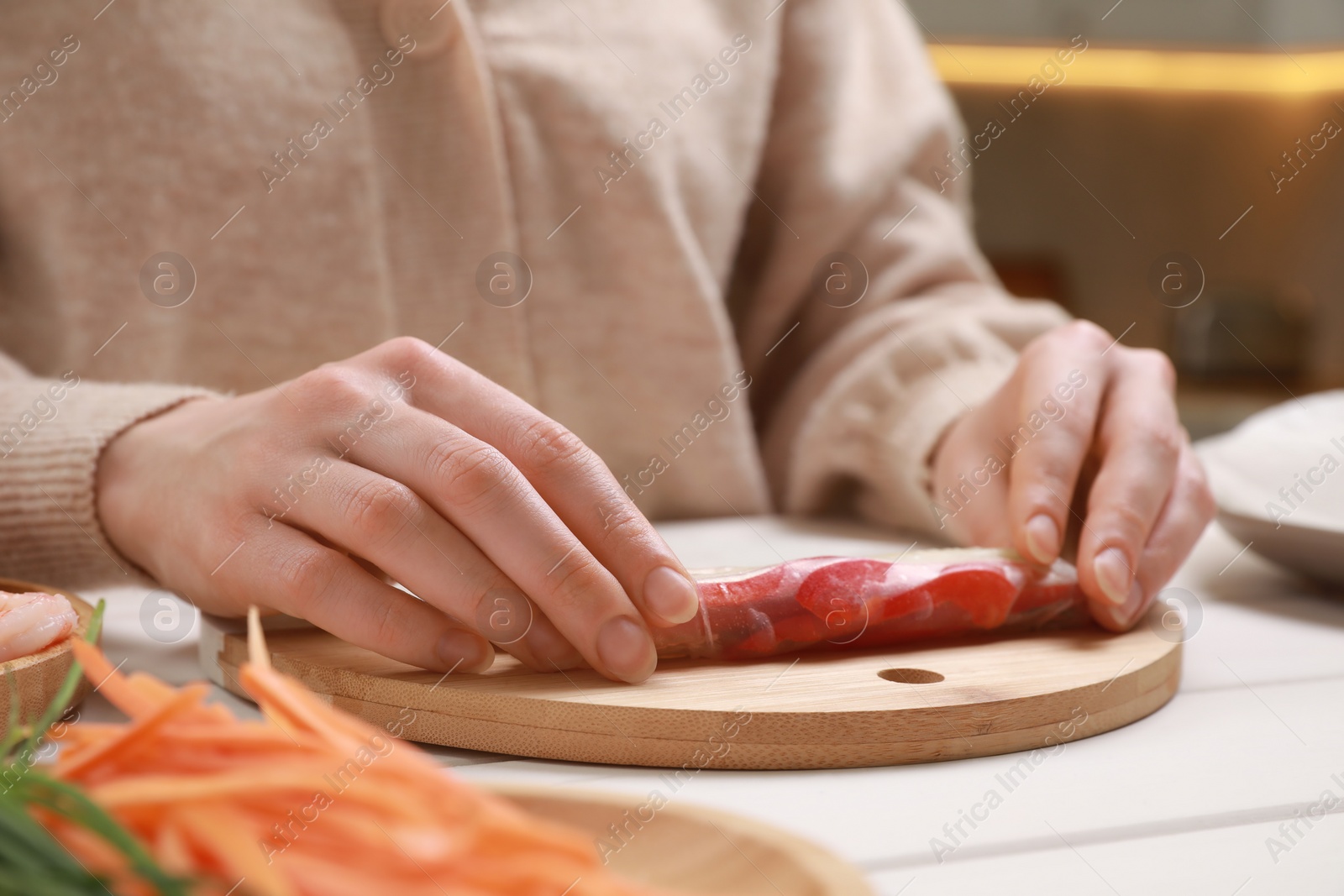 Photo of Woman making delicious spring roll at white wooden table, closeup