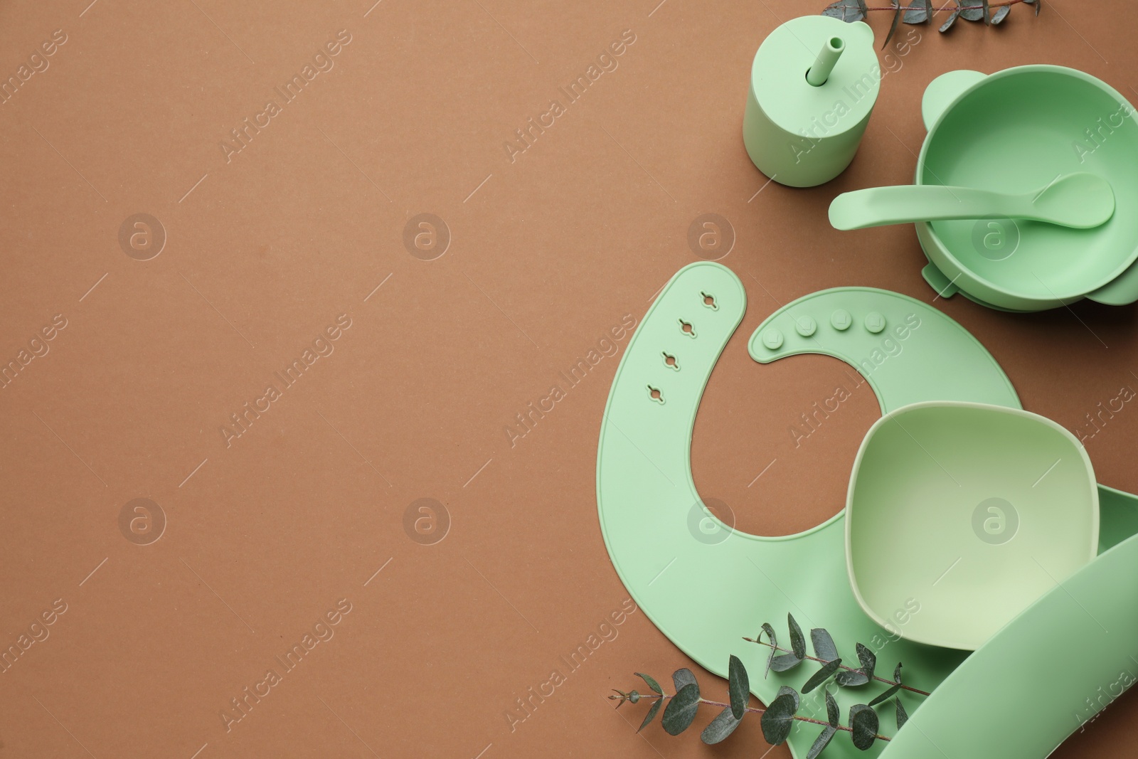 Photo of Flat lay composition with baby feeding accessories and bib on brown background, space for text