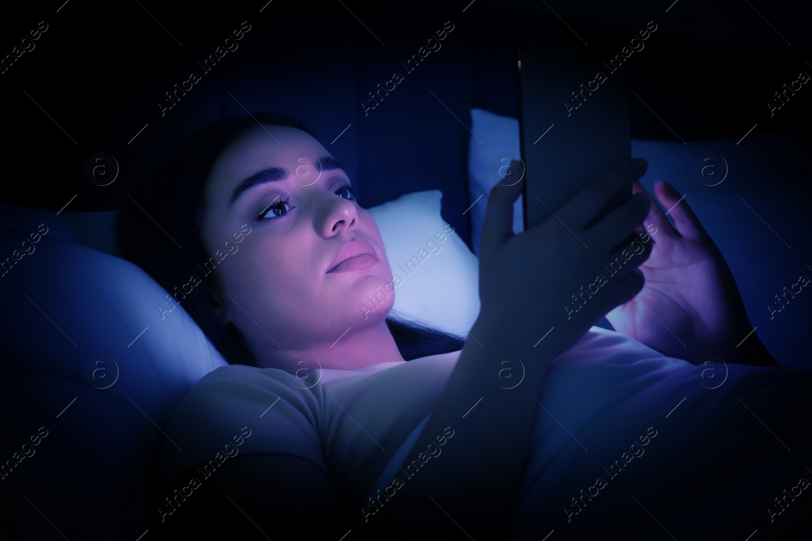 Image of Internet addiction. Woman using smartphone on bed at night. Toned in blue