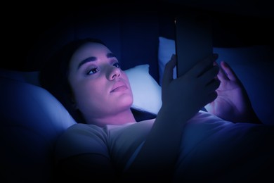 Internet addiction. Woman using smartphone on bed at night. Toned in blue