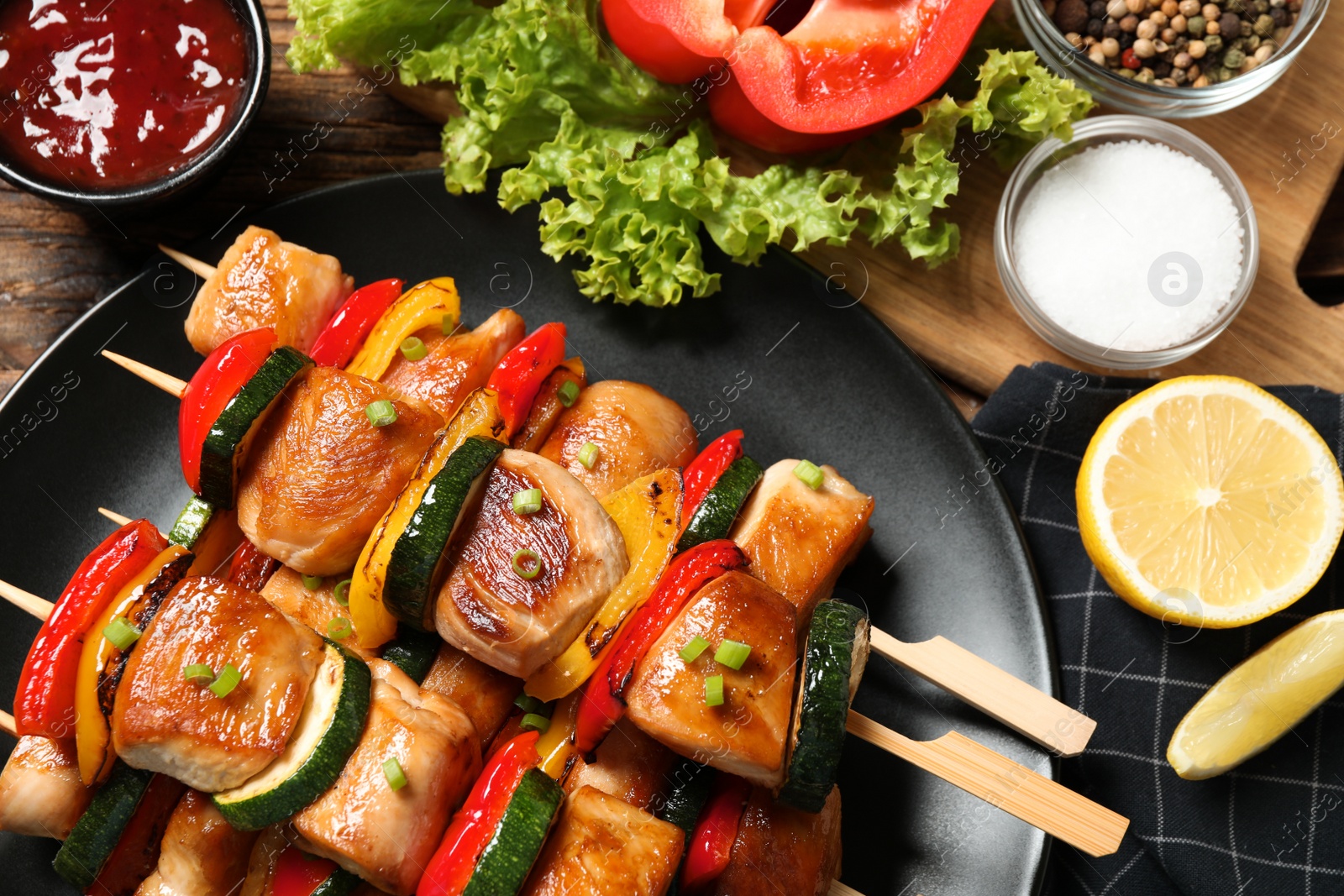 Photo of Delicious chicken shish kebabs with vegetables and lemon on wooden table, closeup