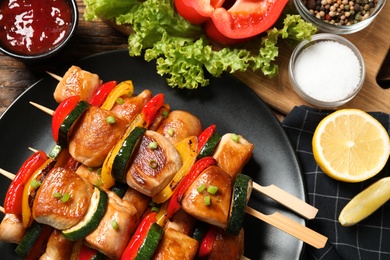 Photo of Delicious chicken shish kebabs with vegetables and lemon on wooden table, closeup