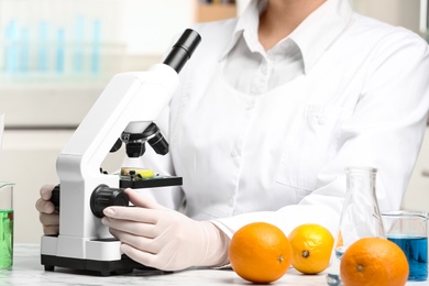 Photo of Scientist inspecting slice of apple with microscope in laboratory, closeup. Poison detection