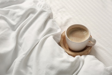 Cup of aromatic coffee on bed with soft blanket, closeup. Space for text