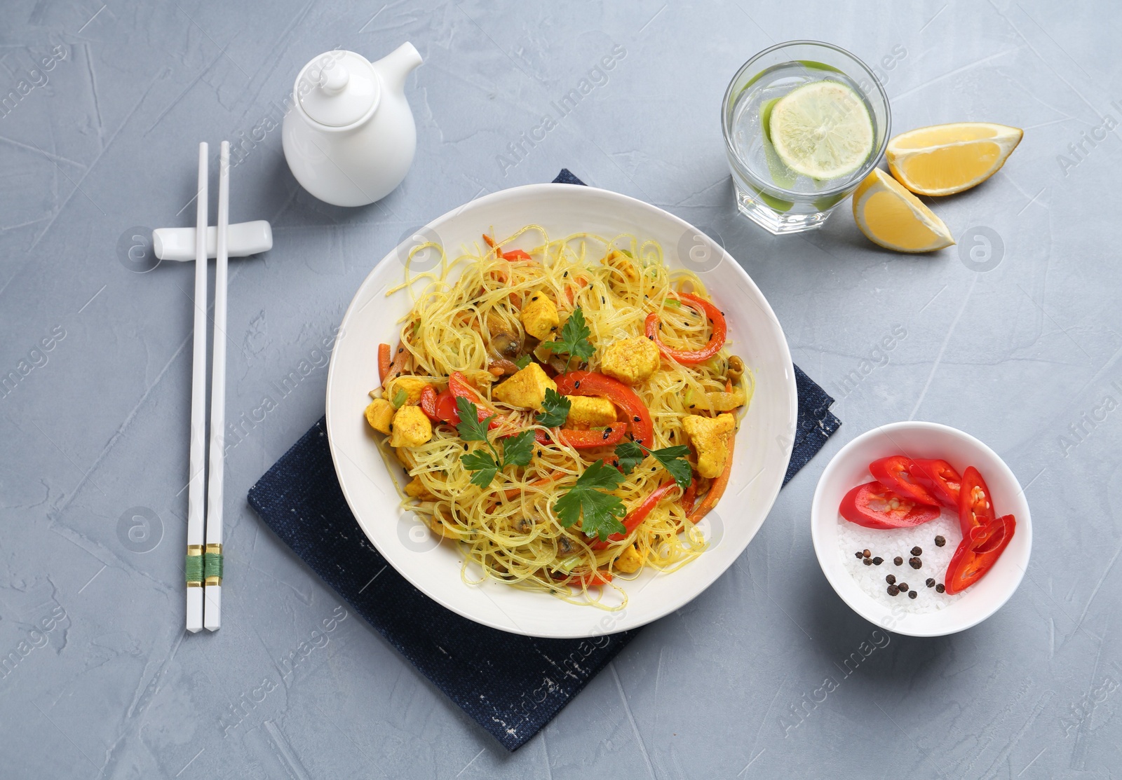 Photo of Stir-fry. Delicious cooked noodles with chicken and vegetables in bowl served on gray textured table, flat lay