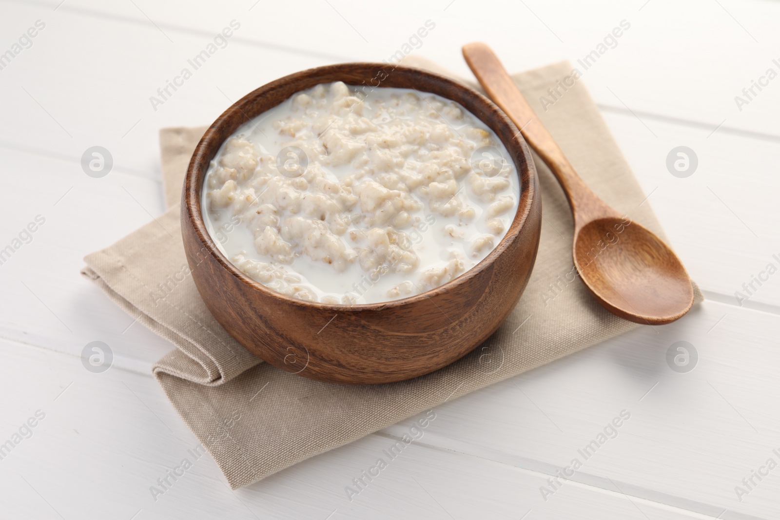 Photo of Tasty boiled oatmeal in bowl and spoon on white wooden table