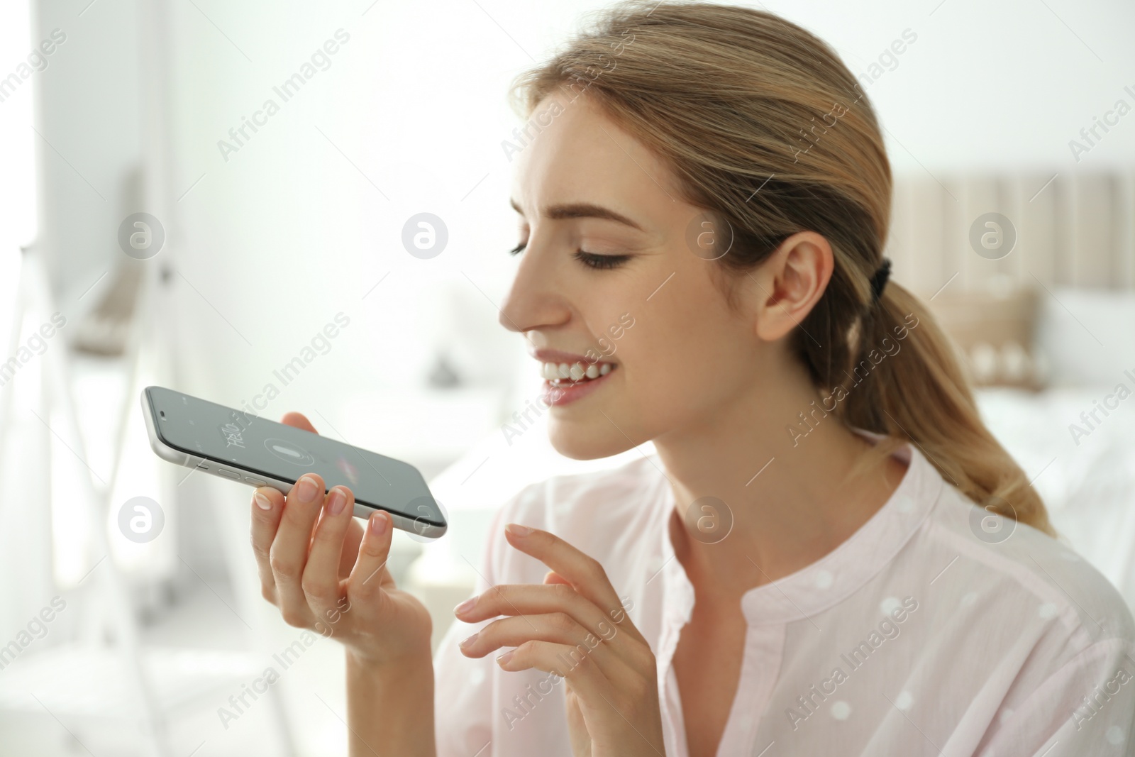 Photo of Young woman using voice search on smartphone indoors