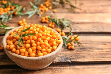 Photo of Fresh ripe sea buckthorn in bowl on wooden table. Space for text