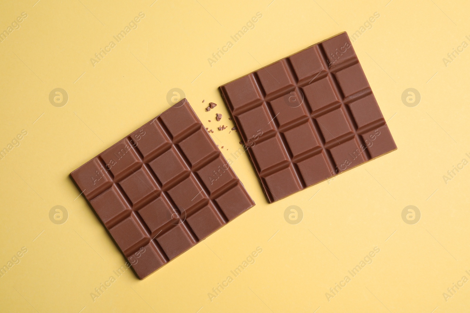 Photo of Pieces of tasty milk chocolate bar on pale yellow background, flat lay
