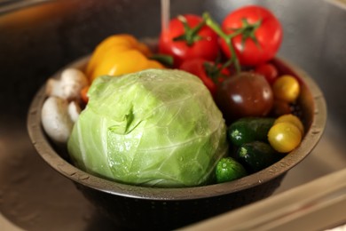 Washing different vegetables with tap water in metal colander inside sink, closeup