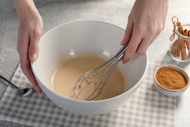 Woman whipping ingredients with whisk at light grey table, closeup. Cooking delicious eggnog