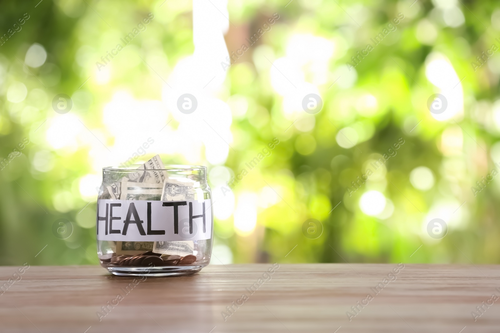 Photo of Glass jar with money and word HEALTH on table against blurred background, space for text