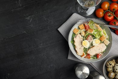 Photo of Delicious Caesar salad in bowl on black table, flat lay. Space for text