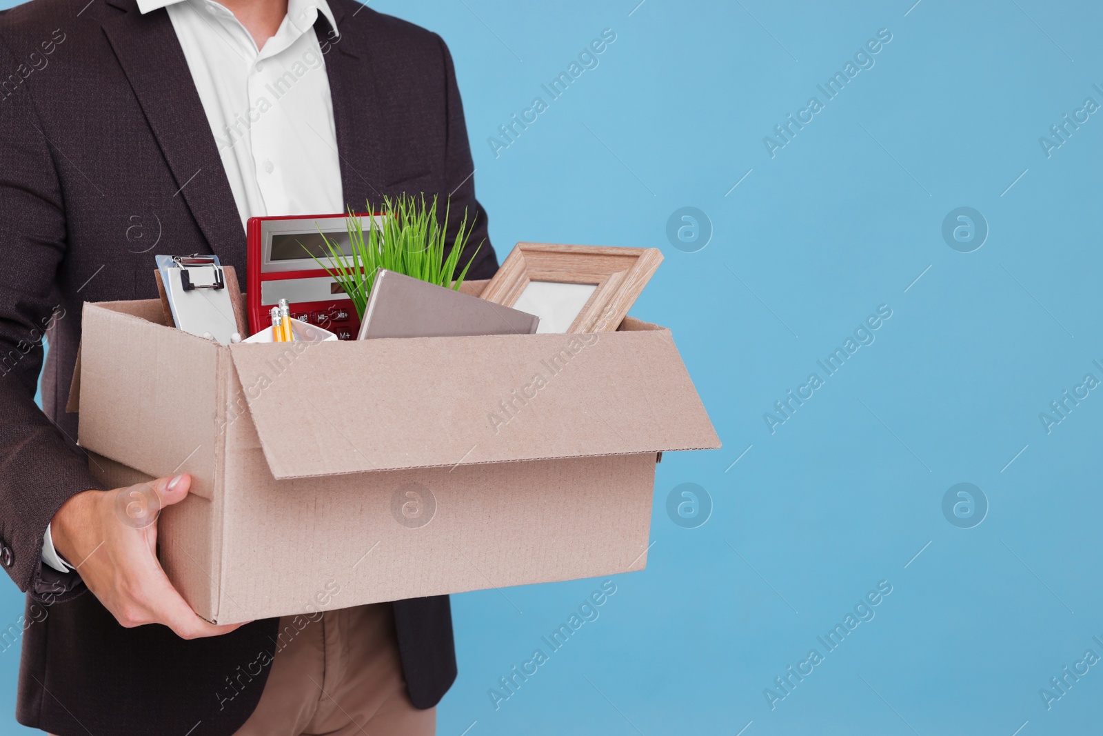 Photo of Unemployed man with box of personal office belongings on light blue background, closeup. Space for text
