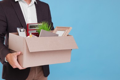 Unemployed man with box of personal office belongings on light blue background, closeup. Space for text