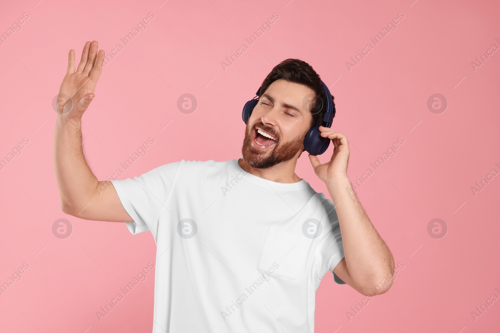 Photo of Emotional man listening music with headphones on pink background