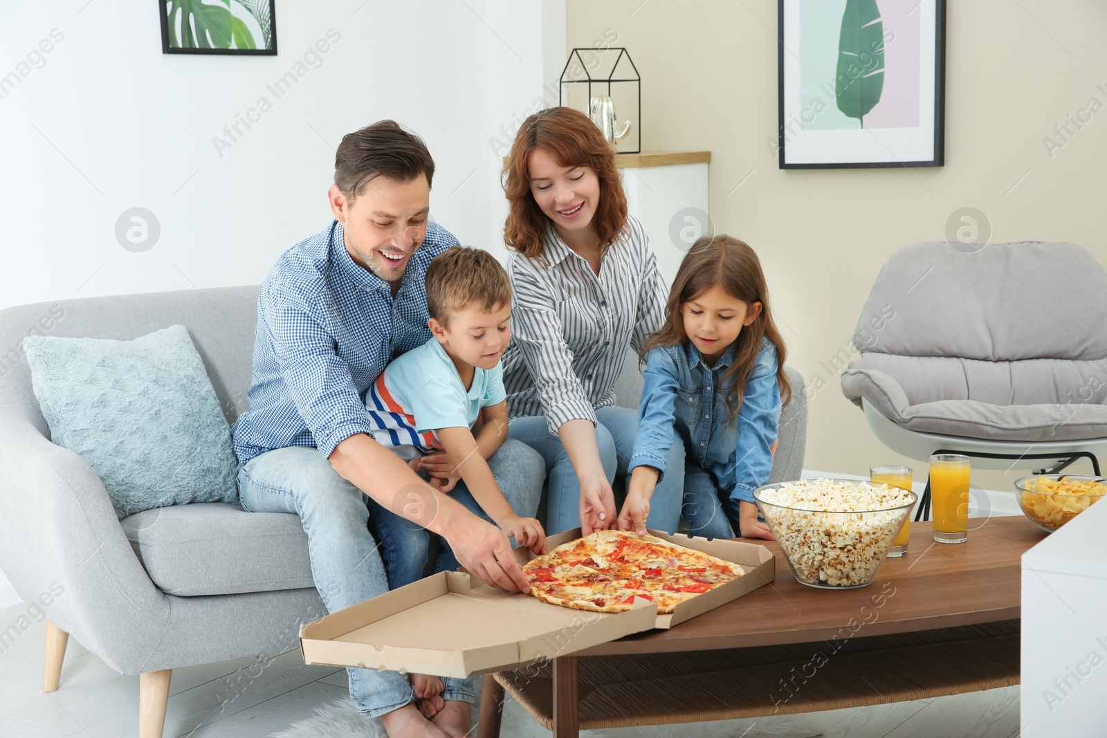 Photo of Family eating pizza while watching TV in room