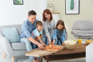 Family eating pizza while watching TV in room