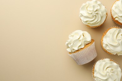 Tasty vanilla cupcakes with cream on beige background, top view. Space for text