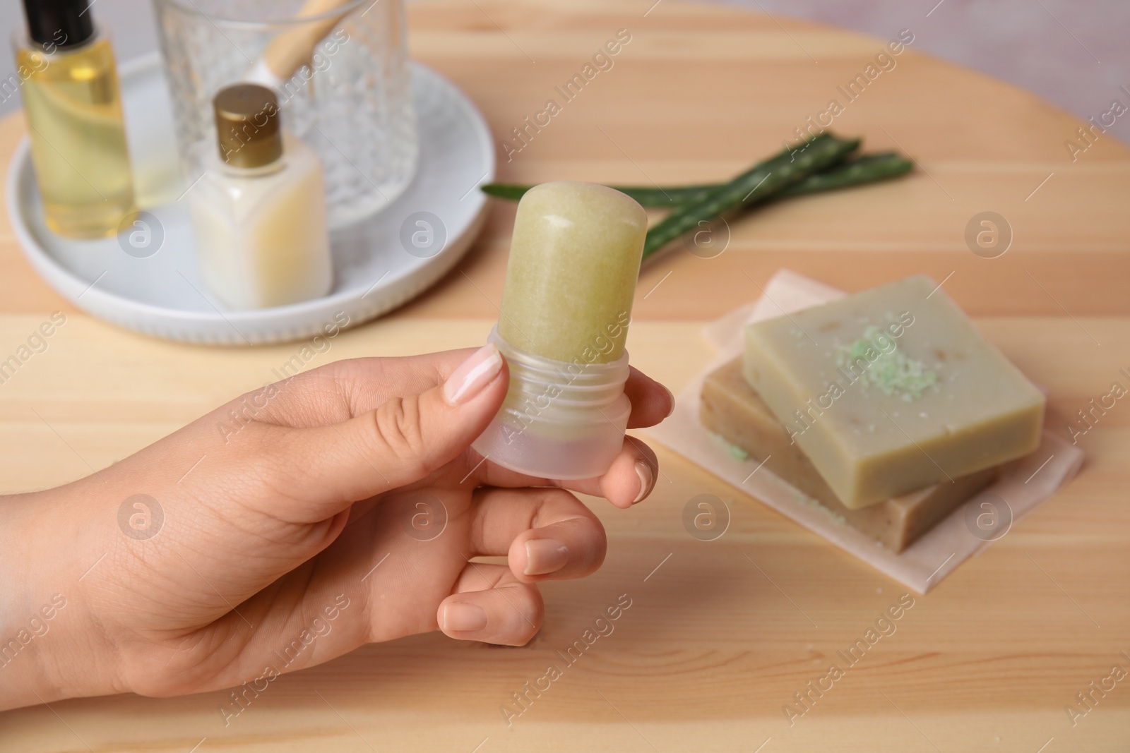 Photo of Young woman holding natural crystal alum deodorant at wooden table, closeup