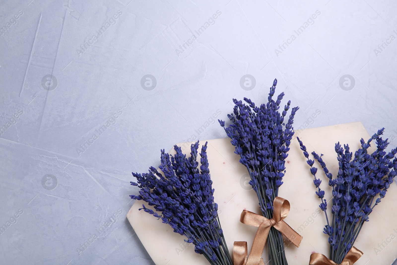 Photo of Bouquets of beautiful preserved lavender flowers and stone board on light grey textured table, top view. Space for text