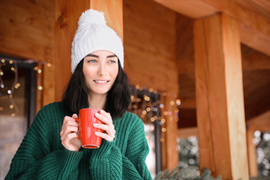 Pretty woman wearing sweater with cup near wooden terrace in winter