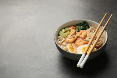 Delicious ramen with shrimps and chopsticks on grey table, space for text. Noodle soup