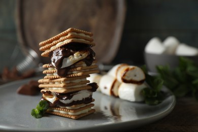 Photo of Delicious marshmallow sandwiches with crackers and chocolate on grey plate, closeup. Space for text