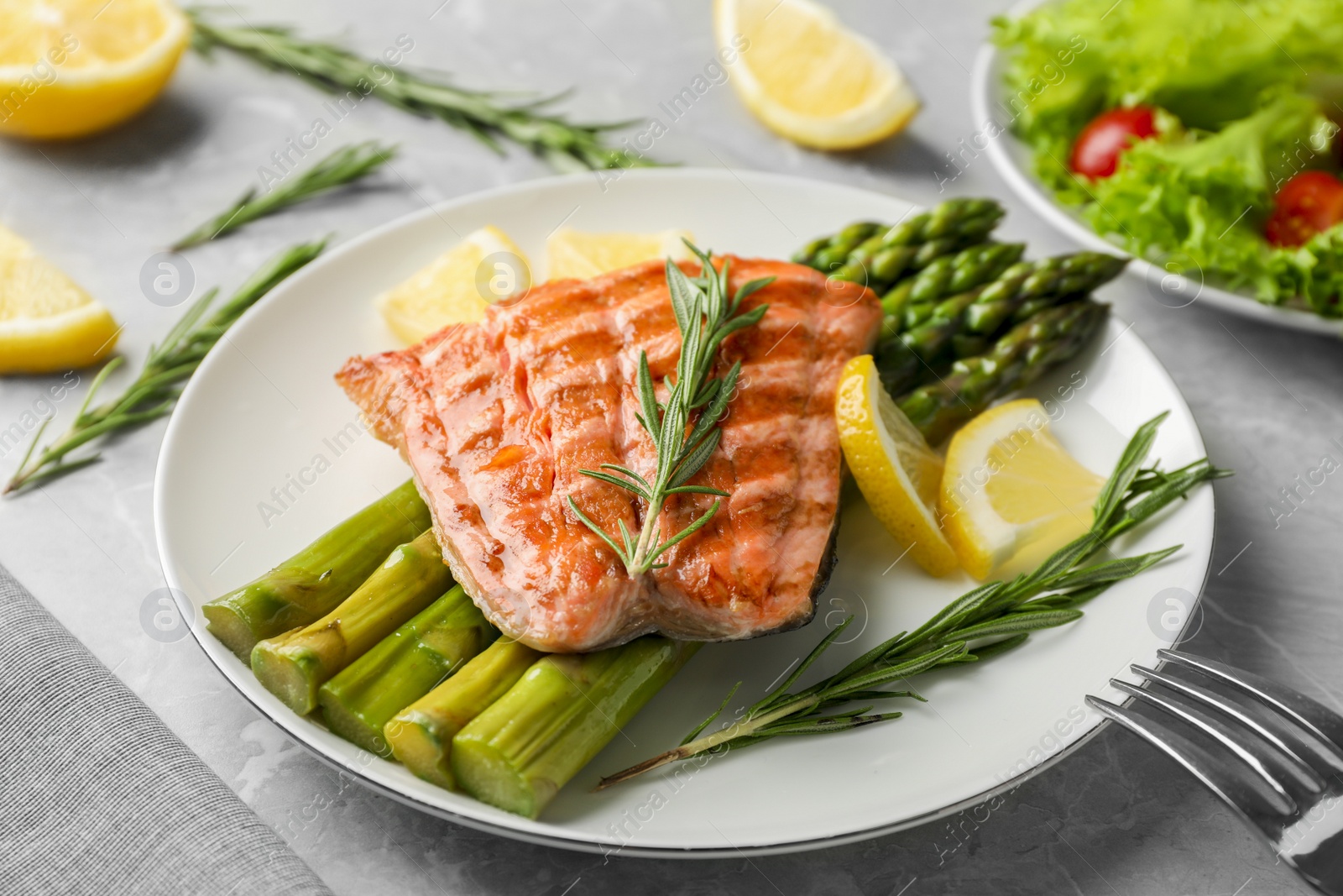 Photo of Tasty grilled salmon with asparagus, lemon and rosemary on light grey table