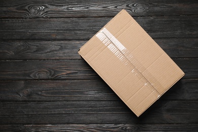 Photo of Closed cardboard box on black wooden background, top view. Space for text