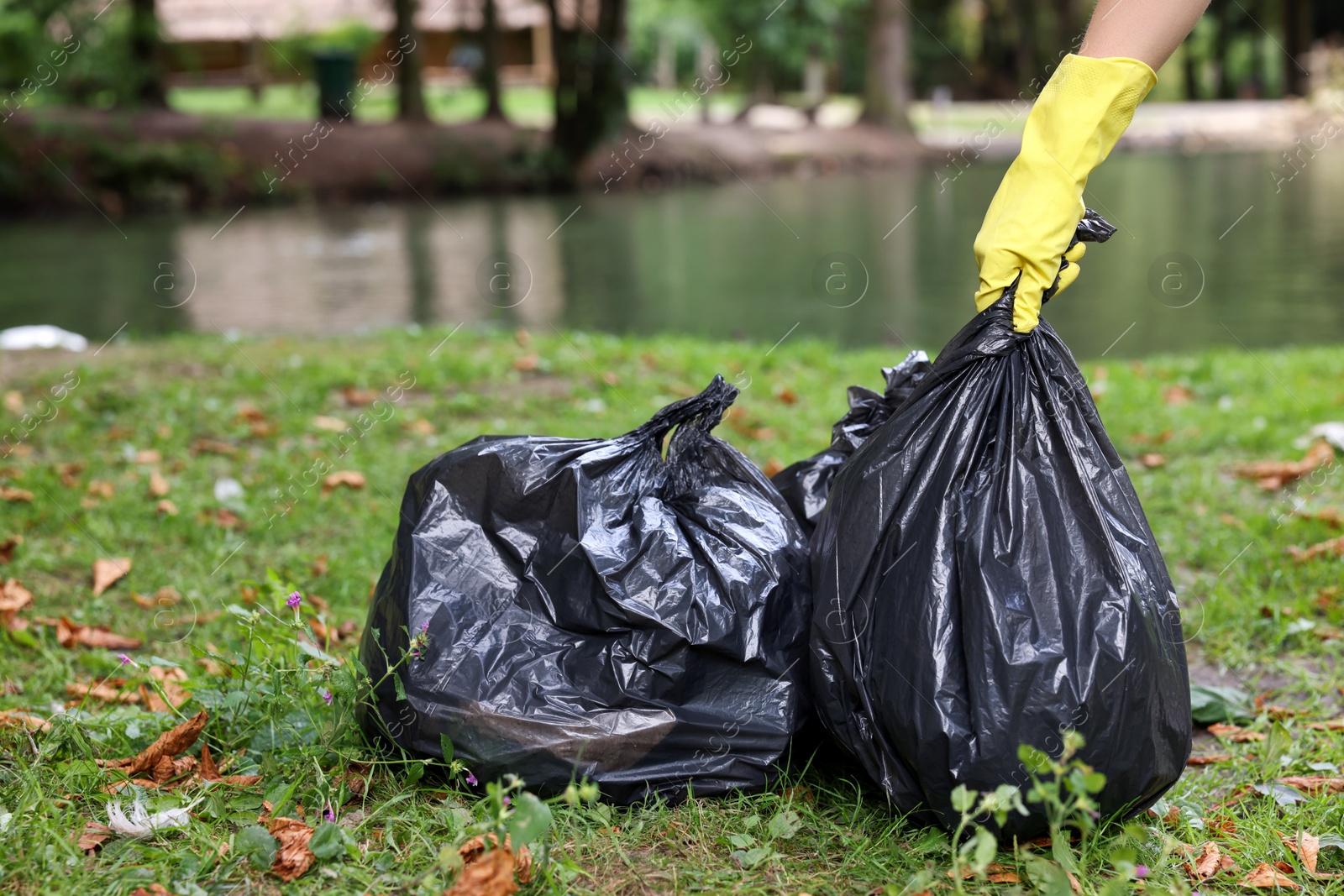 Photo of Woman holding plastic bags with garbage in park, closeup.