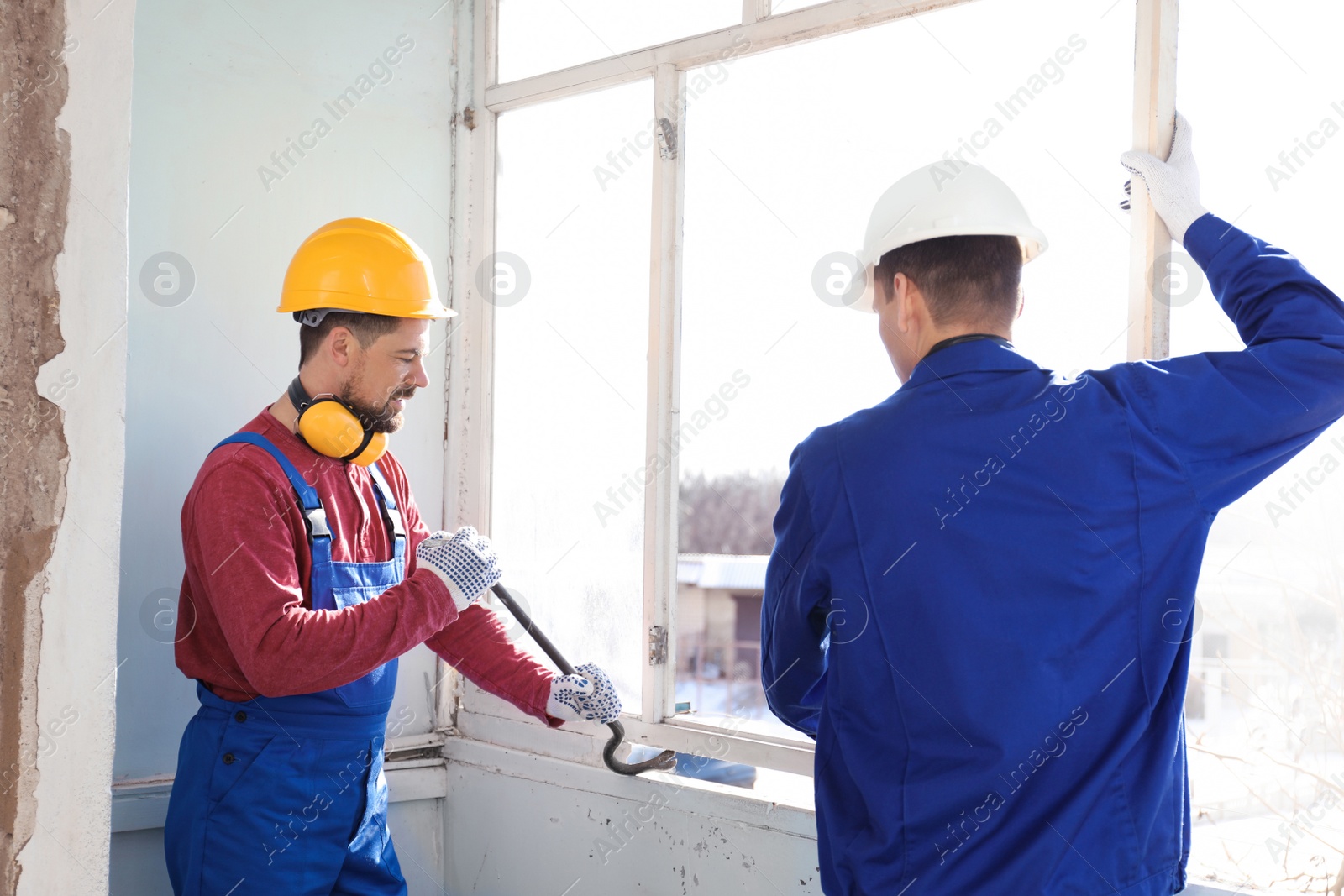 Photo of Workers dismantling old window with crowbar indoors