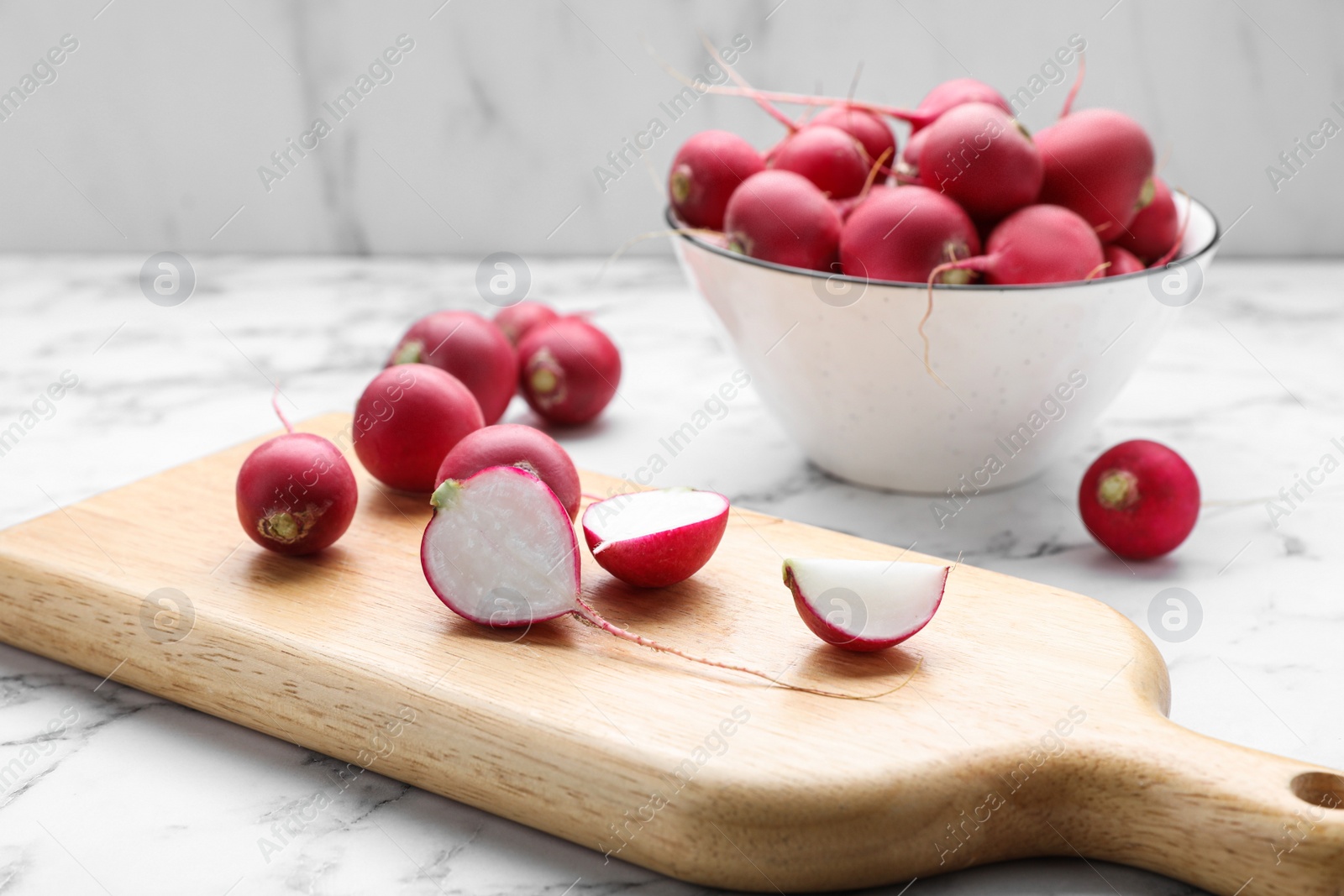 Photo of Board and bowl with fresh ripe radishes on white marble table