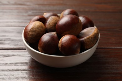 Photo of Sweet fresh edible chestnuts in bowl on wooden table, closeup