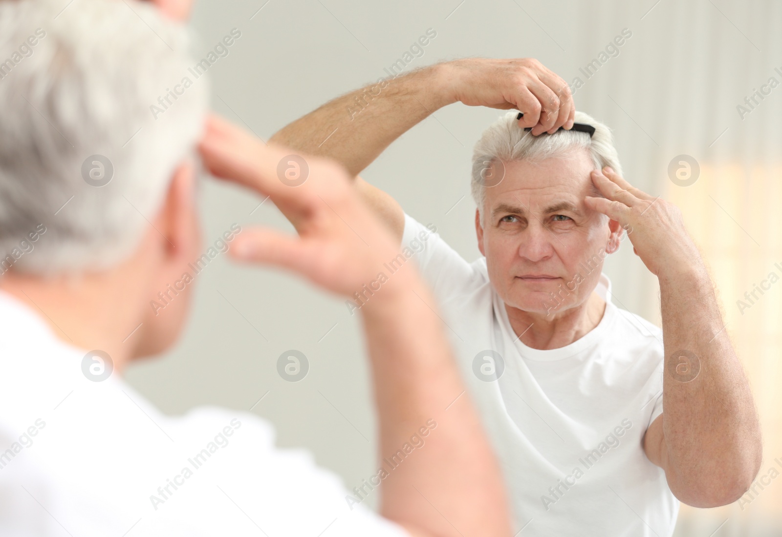 Photo of Senior man with hair loss problem looking in mirror indoors