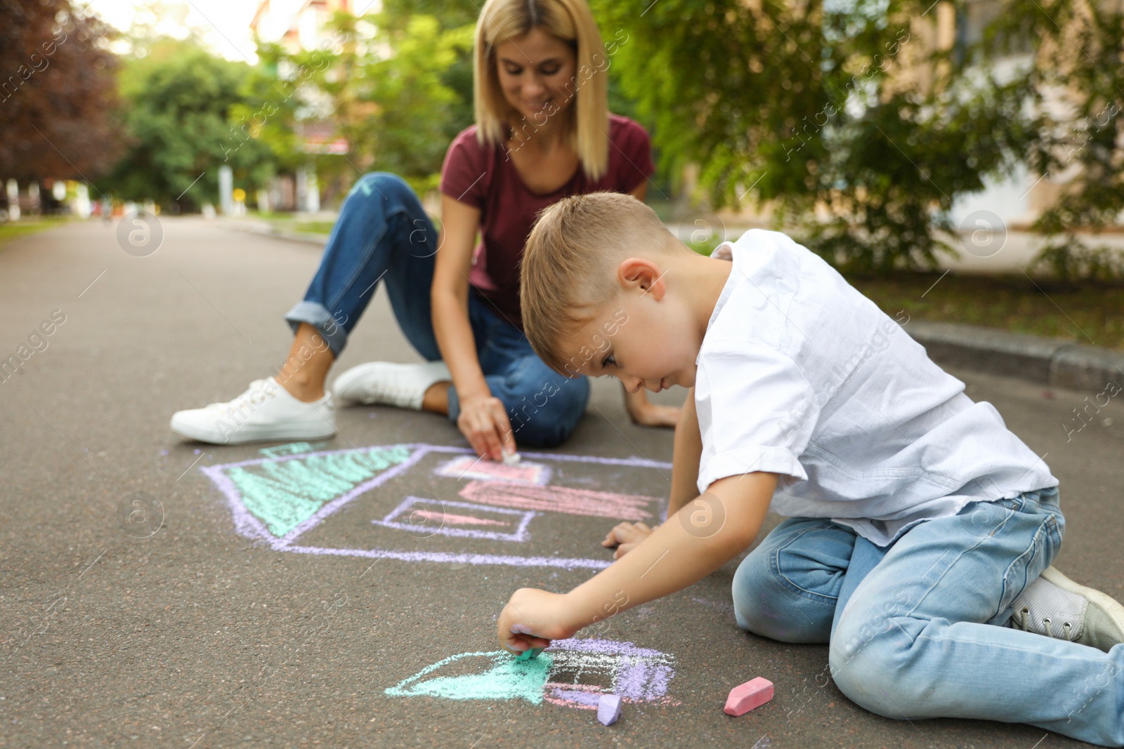 Photo of Nanny with cute little boy drawing house with chalks on asphalt