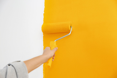 Photo of Woman painting white wall with yellow dye, closeup. Interior renovation