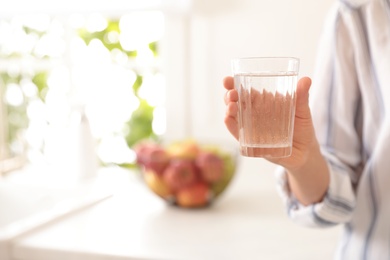 Young woman holding glass of pure water in kitchen, closeup. Space for text