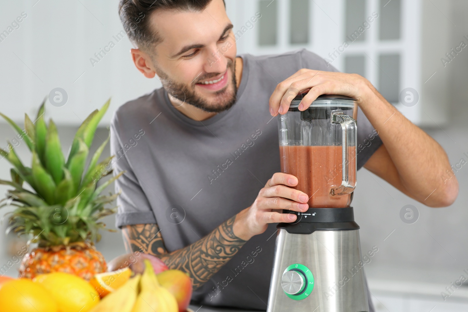 Photo of Handsome man preparing tasty smoothie in kitchen, focus on blender