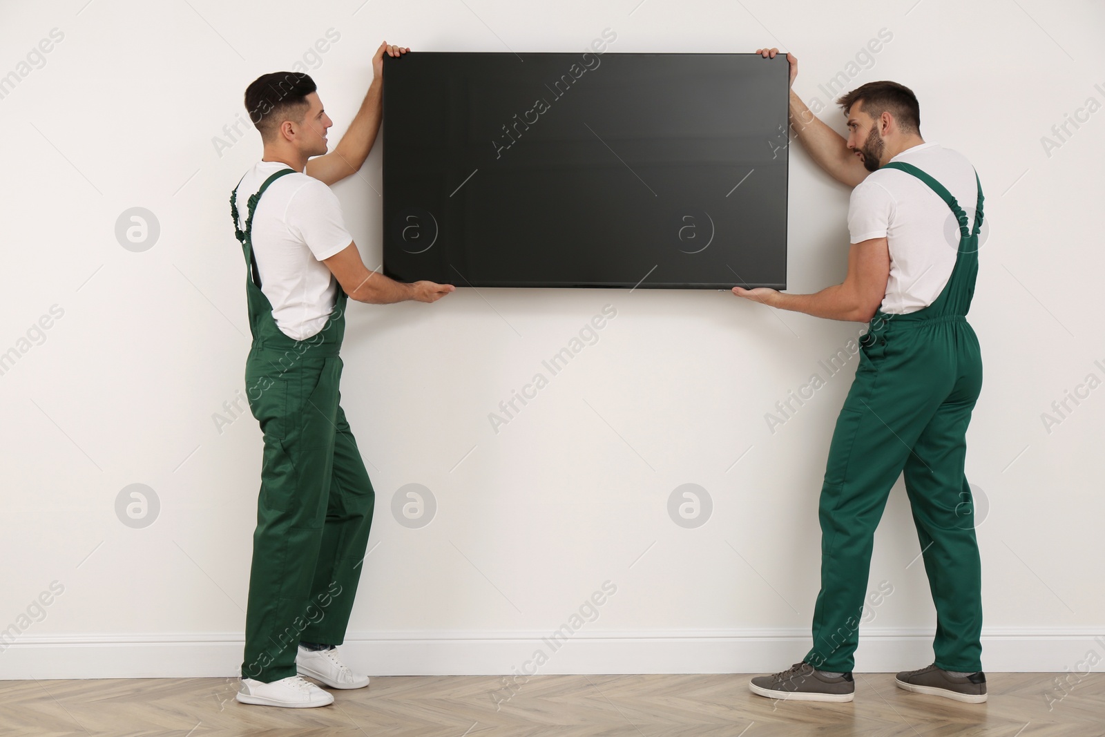 Photo of Professional technicians installing modern flat screen TV on wall indoors