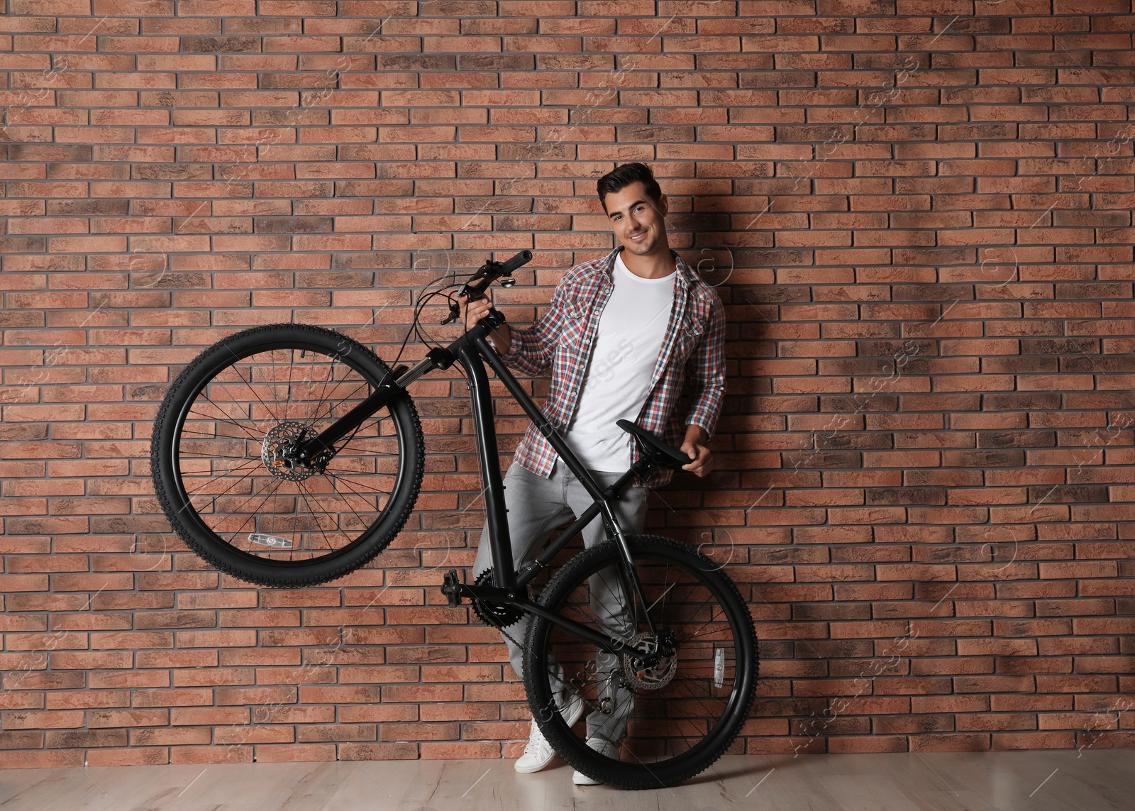 Photo of Handsome young man with modern bicycle near brick wall indoors