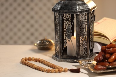 Photo of Arabic lantern, Quran, misbaha and dates on white table. Space for text