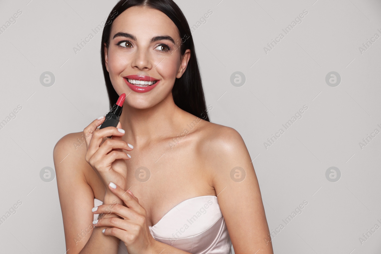 Photo of Young woman with beautiful makeup holding glossy lipstick on light gray background, space for text