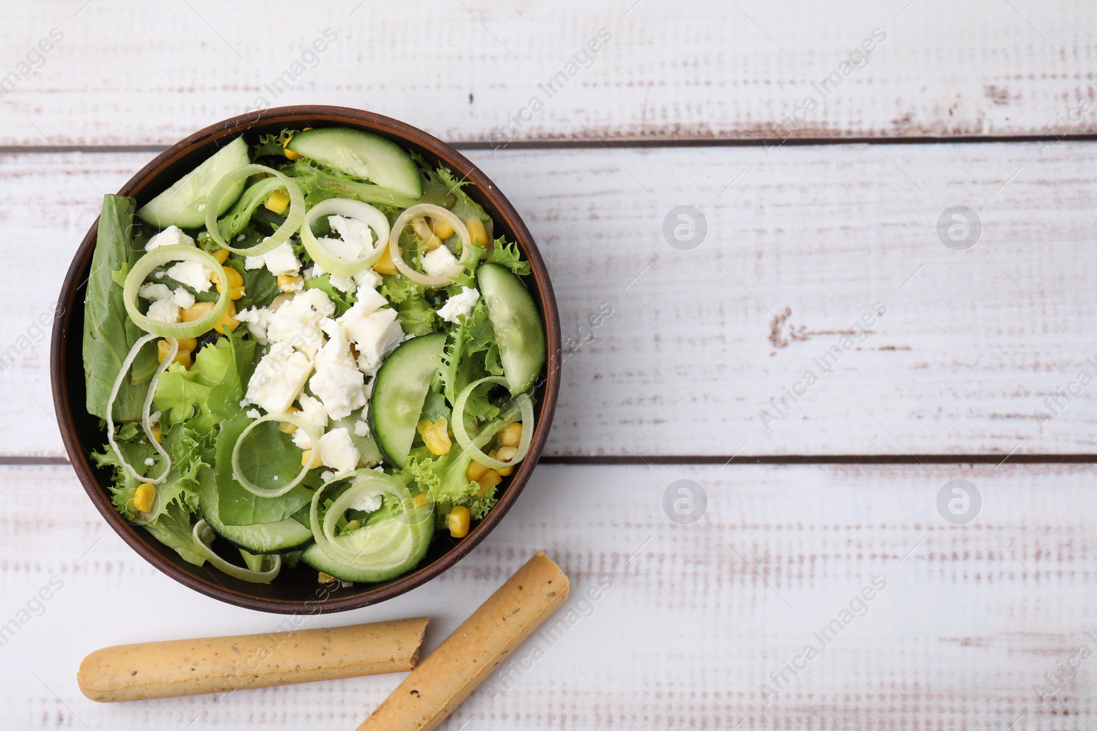 Photo of Bowl of tasty salad with leek, cheese and grissini on white wooden table, top view. Space for text