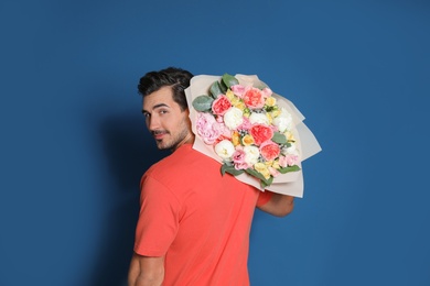 Photo of Young handsome man with beautiful flower bouquet on blue background