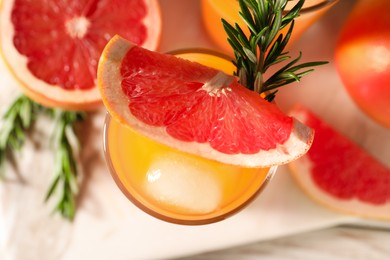 Photo of Tasty grapefruit drink with ice in glass, rosemary and fresh fruits on light table, top view