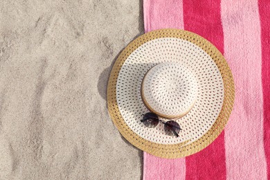Beach towel with straw hat and sunglasses on sand, flat lay. Space for text
