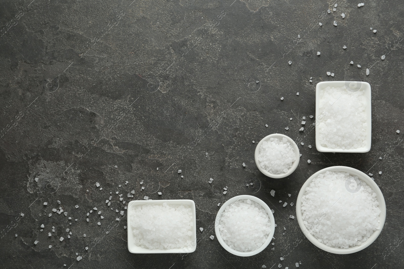 Photo of Bowls with natural sea salt on grey table, flat lay. Space for text