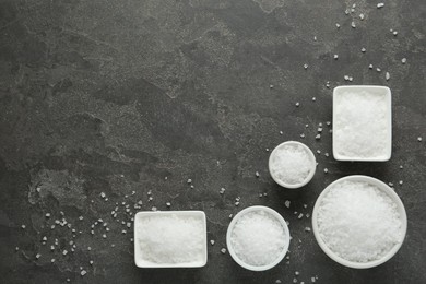 Bowls with natural sea salt on grey table, flat lay. Space for text