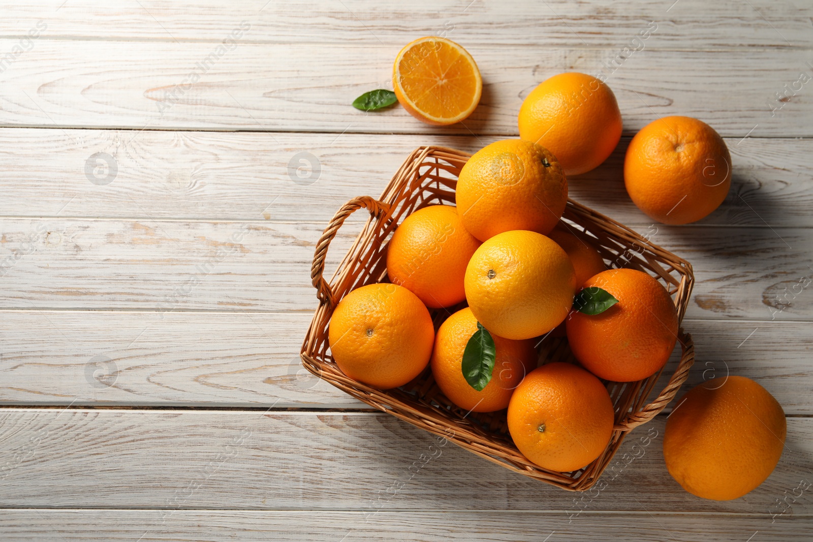 Photo of Many ripe oranges and green leaves on wooden table, top view. Space for text